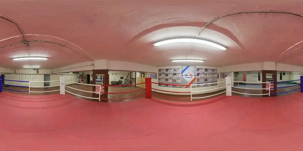 Sala de treino de boxe com ringue montado junto a paredes em tons quentes